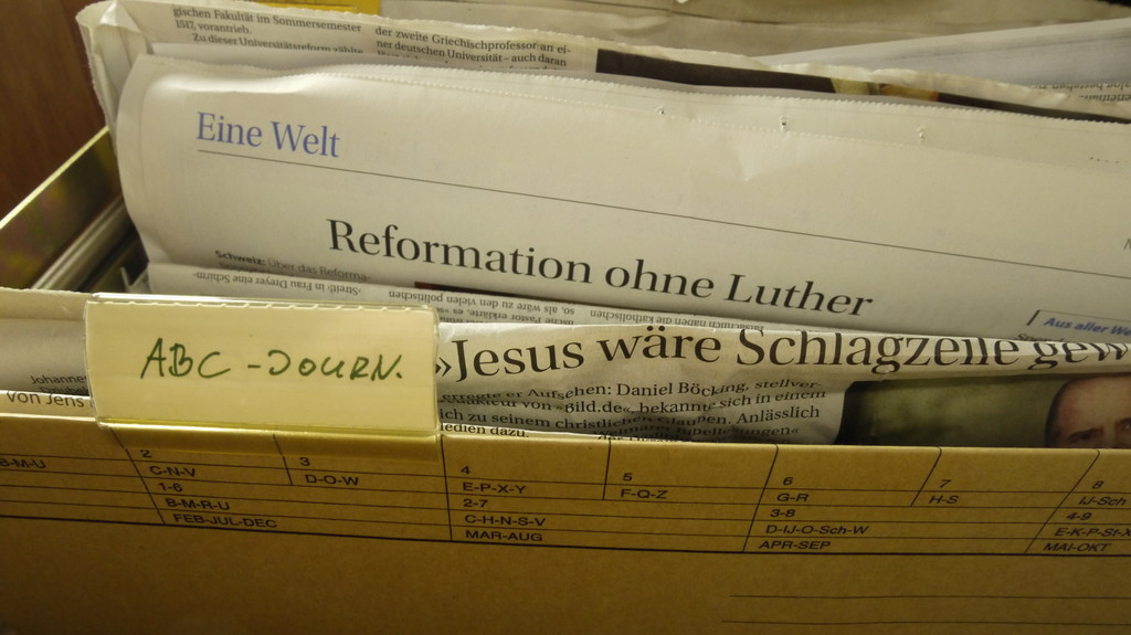 Hängeregistratur mit Zeitungsausschnitten. Beschirtung ABC-Journal. SIchtbare Überschriften auf Zeitungen: Reformation ohne Luther, Jesus wäre Schlagzeile