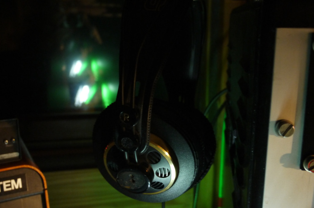Im Vordergund ist ein Kopfhörer zu sehen, im Hintergrund spiegeln sich grüne Lichter