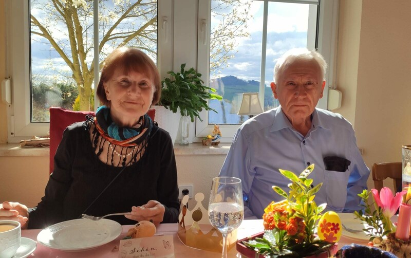 Waltraud und Manfred Rücker sitzen an einer Festtafel. Sie schauen direkt in die Kamera. Im Vordergund bunte Blumengestecke