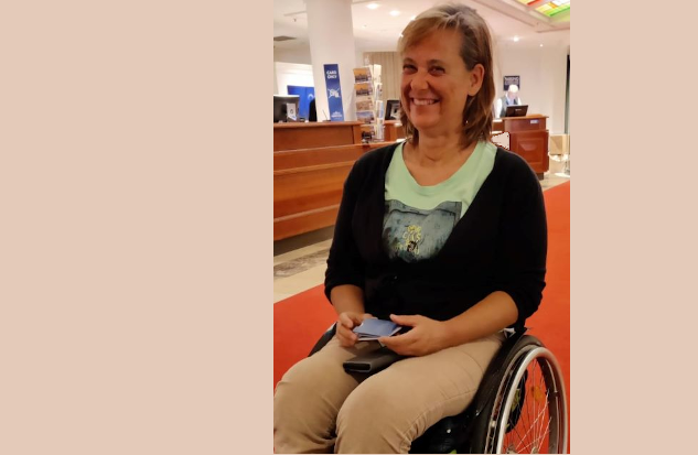 Martina Köninger sitzt fröhlich im Rollstuhl im Foyer eines Niederländischen Hotels bei einem Treffen mit evakuierten ukrainischen behinderten Menschen