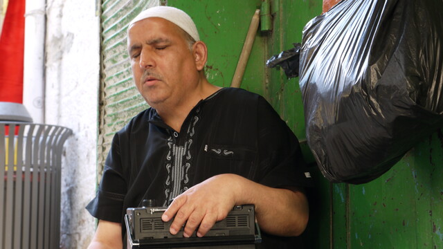 Ein blinder Mann sitzt in einer Gasse der Altstadt von Jerusalem und hört Kofferradio