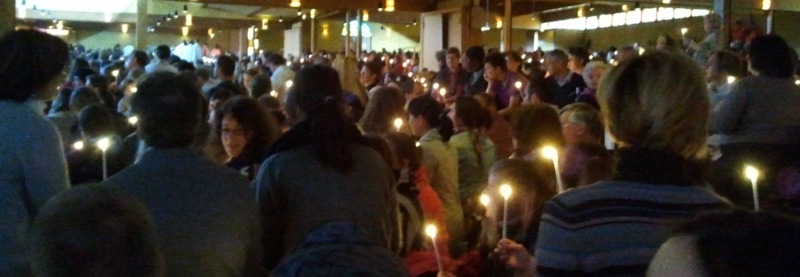 Viele junge Leute halten oider reichen ds Osterlicht mit Kerzen in der Kirche zu Taizé weiter 