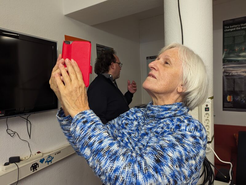 Gudrun Uhlig schwenkt das Smartphone in verschiedene Richtungen und erkundet mit einer mobilen App den ihr fremden Raum, um sich darin orientieren zu können.