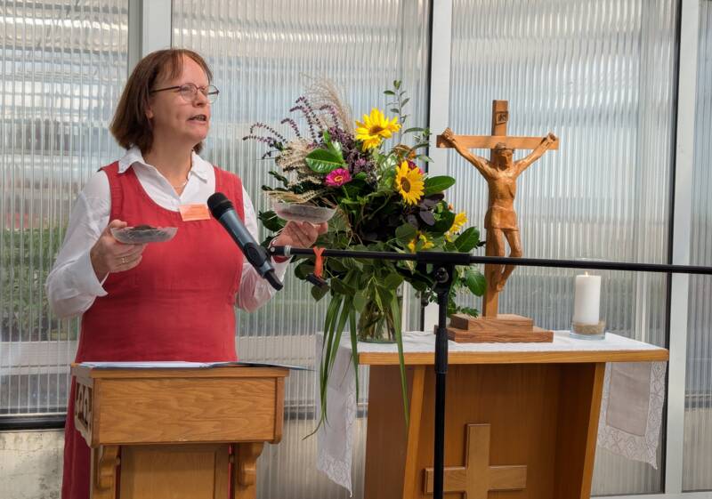 Pfarrerin Fourestier steht mit zwei Schalen voll Erde vor einem improvisierten Altar mit Blumen und Kreuz.