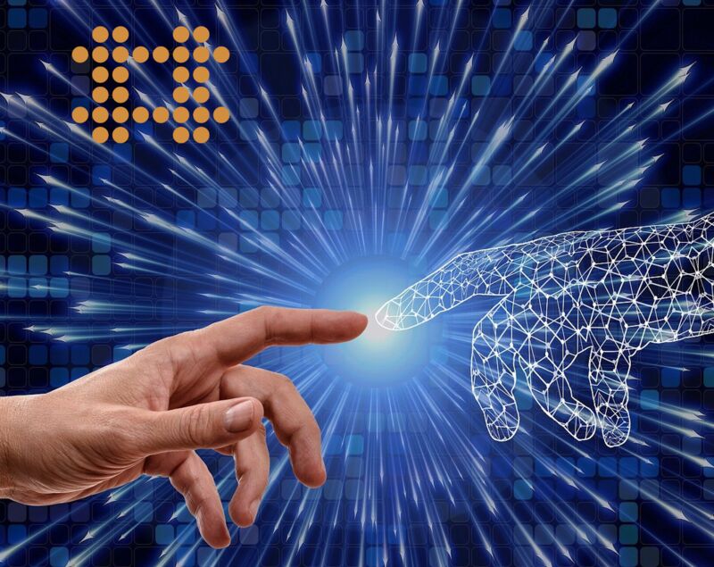 Die Zeigefinger zweir Hände berühren sich an den Spitzen. Die eine Hand ist als menschliche Hand zu erkennen, die Andere ist symbolisch als digitales Raster gestaltet. Oben links sind die (Punktschriftpunkte) aus dem Logo des KOM-IN-Netzwerkes zu sehen